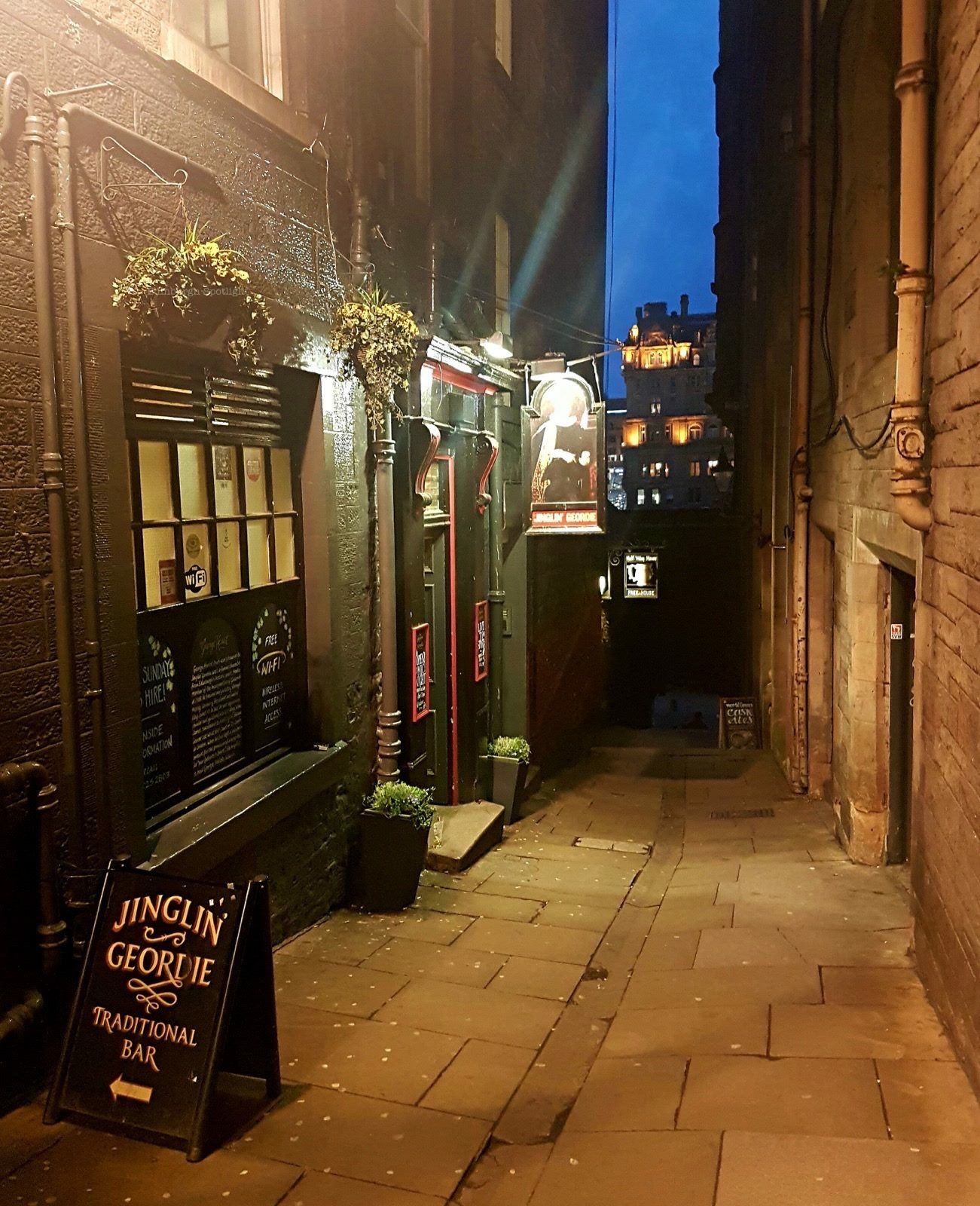The pub’s door and window at dusk, with the A-board on the close and the hanging sign lit above