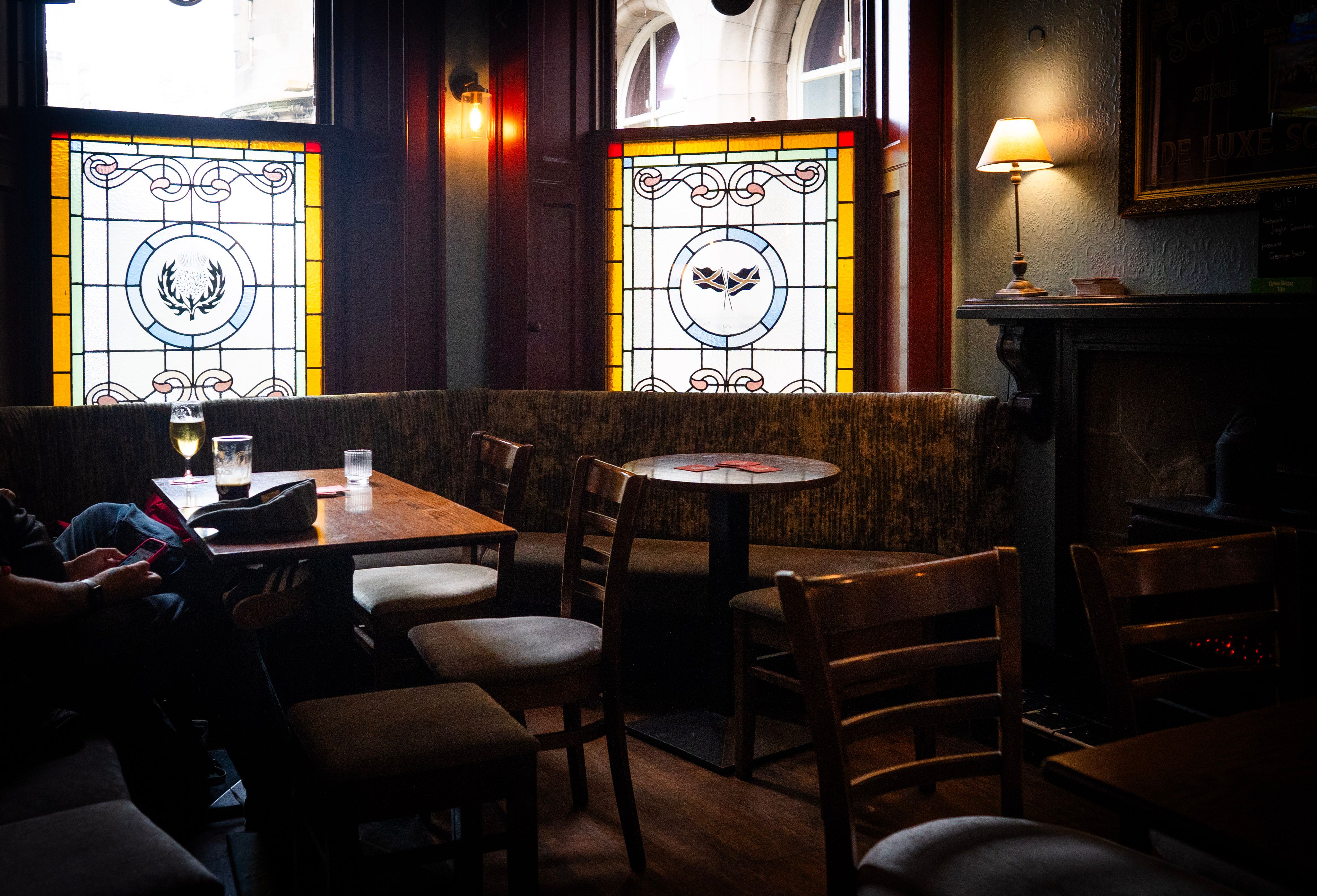 The lounge, with two of the four stained glass panels in the windows, a man reading at a table and the fireplace on the right