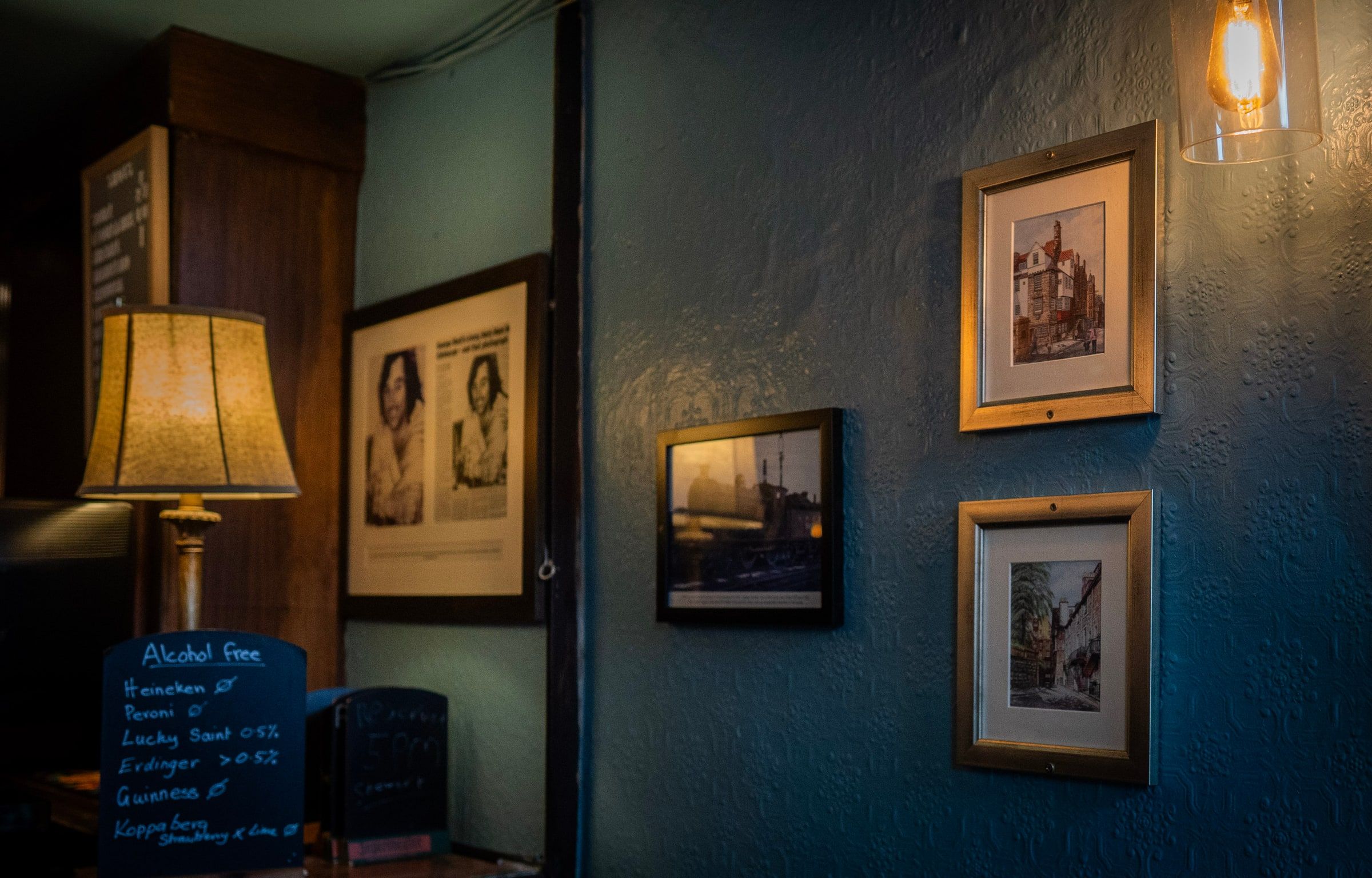 A lamp, a chalkboard of alcohol free drinks and framed pictures of old Edinburgh on the blue wall of the lounge